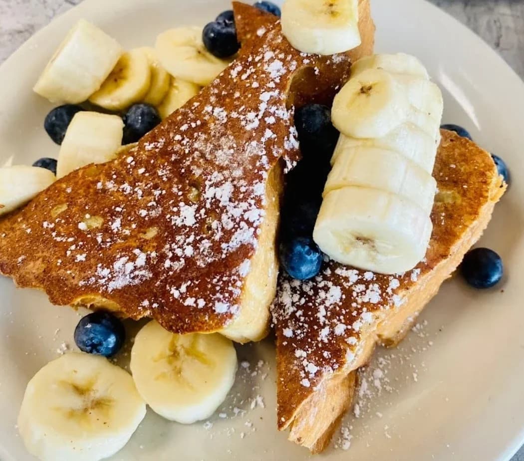 Thick-cut French toast dusted with powdered sugar, served with fresh bananas and blueberries at Maria's Place.