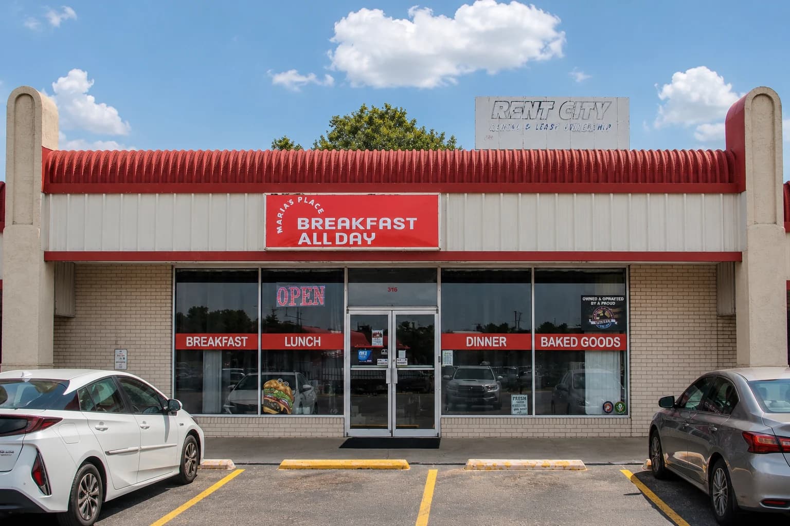 The Maria's Place storefront: a cream brick unit with a red corrugated awning and a red sign reading Maria's Place, Breakfast All Day, above glass double doors.